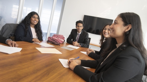 Four students sitting around a wooden conference table talking and smiling with each other