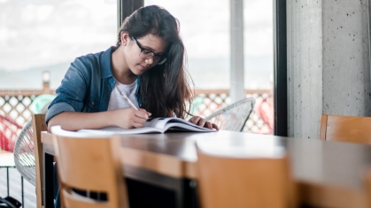 Young woman with glasses and brown hair reading at a long wooden table