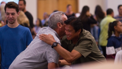 two people at the center of image hugging at a large community meeting