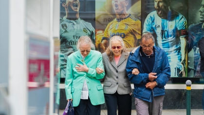 three older adults standing in bus waiting area with image of soccer players in the background