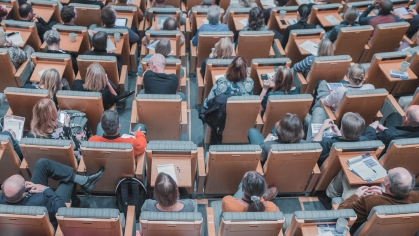 Overhead photo of a large room with many seats. The photo is of the tops of people's heads sitting in the seating