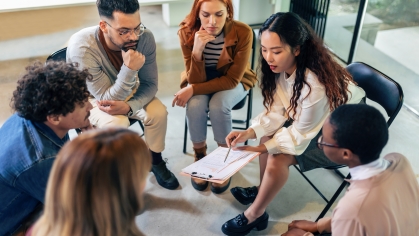 Stock image of people sitting in a circle looking at a document together