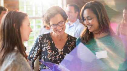 Stock photos of three female presenting people smiling and looking at purple folders