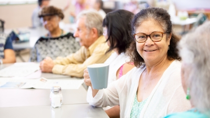 Close up of older adult with coffee mug at table with other older adults