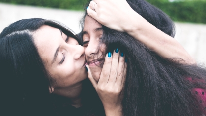 mother kissing teenage daughter on cheek