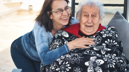 stock image of two women smiling together. one is an older presenting female wrapped in a blanket and sitting in a chair
