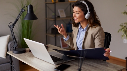 woman with headphones talking to people on a video call on her computer