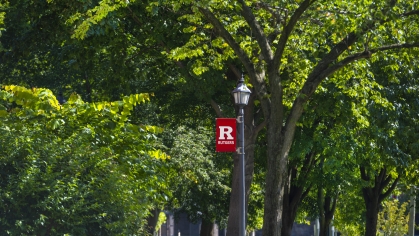 Lamp post with Rutgers R banner among a row of green trees
