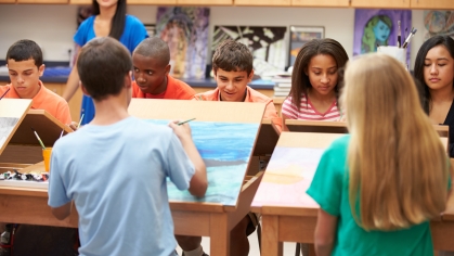 Middle school age children in an art class painting on canvases