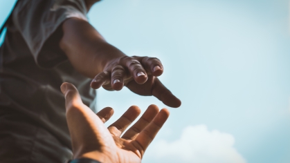 Someone reaching out a hand to lift up another, the camera's point of view is looking up at the person holding out their hand