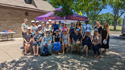 Group of people under event text covered in shade of a tree