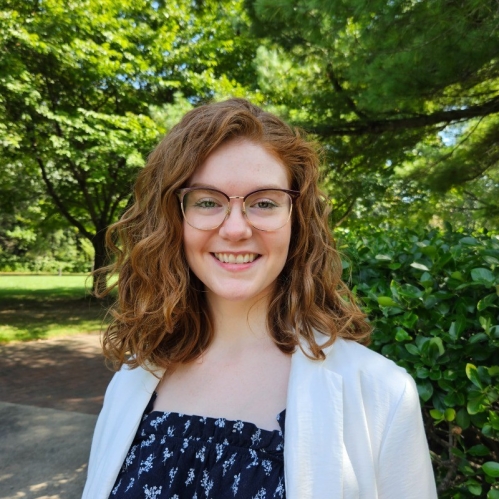 Photo of woman with red hair and glasses in front of trees