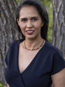 Close photo of a woman in the foreground wearing a dark colored v-neck shirt and smiling at the camera