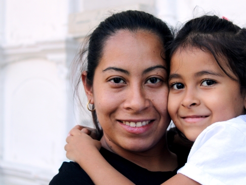 Imagine of a woman and holding her daughter; both are smiling at the camera