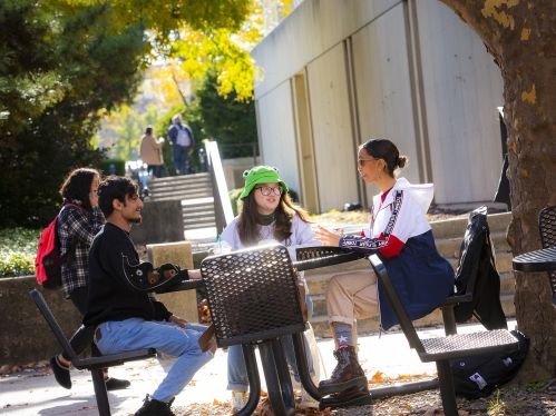 Three students sitting outside at a table under a tree