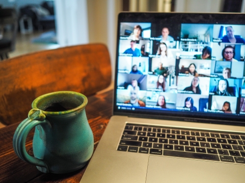 Coffee mug on a table next to a laptop with a Zoom screen open and multiple participants shown