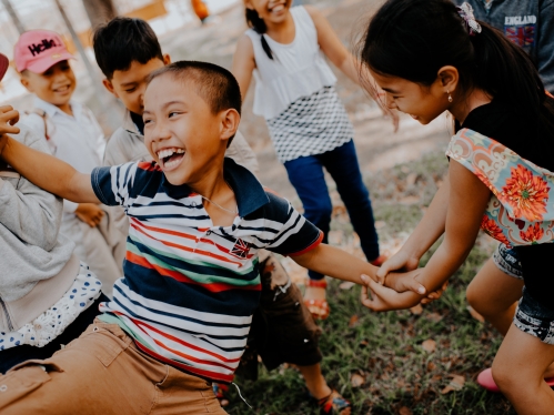 Photo is of young children mostly in a circle laughing with each other