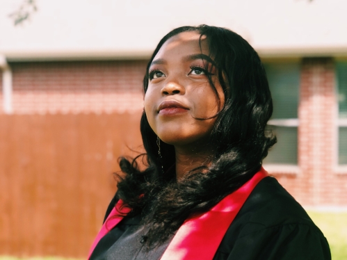Adult Black female student in a black graduation gown with a red ribbon