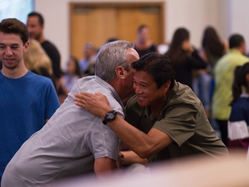 two people at the center of image hugging at a large community meeting