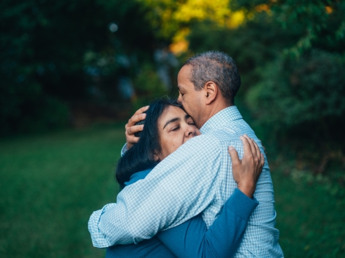 Two adults hugging; one female presenting and one male presenting; comforting embrace