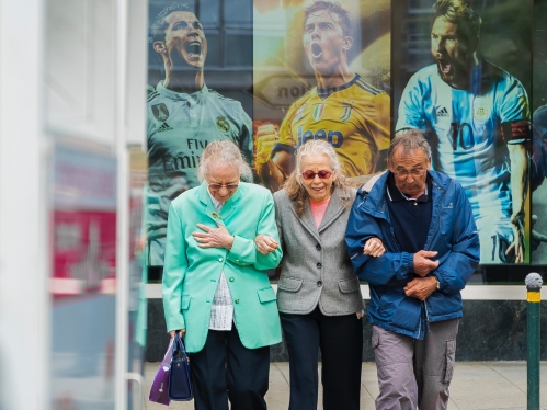 three older adults standing in bus waiting area with image of soccer players in the background