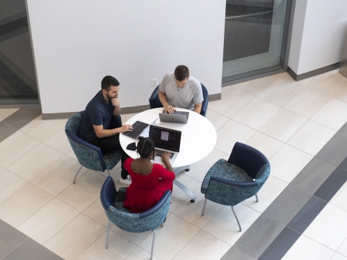 overhead image of three people sitting with their laptops together around a circular table